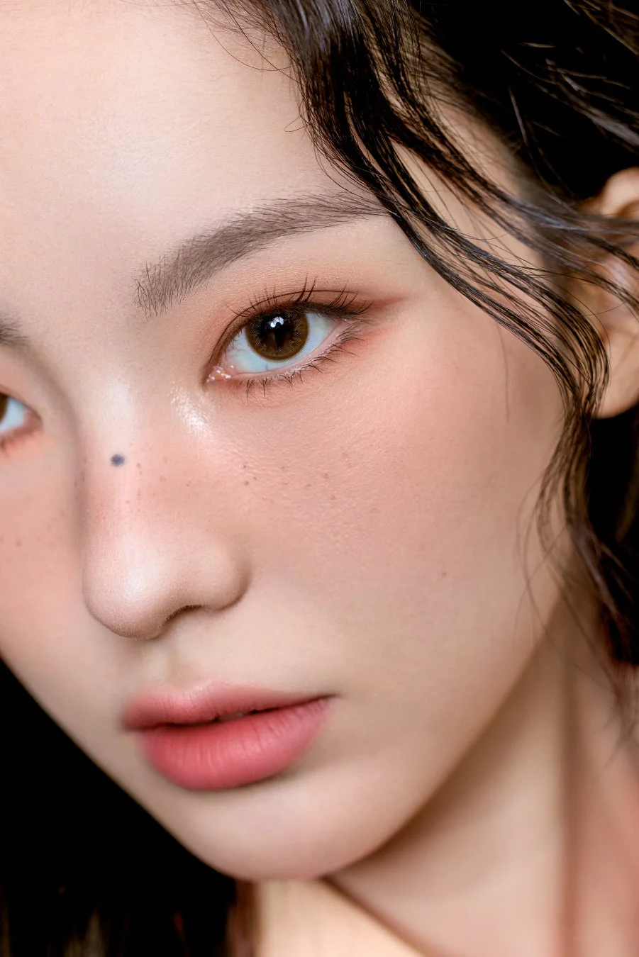 女性の顔のクローズアップ画像。ブラウンのカラコン、ピーチ系のアイシャドウ、ピンク系のリップとチークでナチュラルなメイクが施されています。