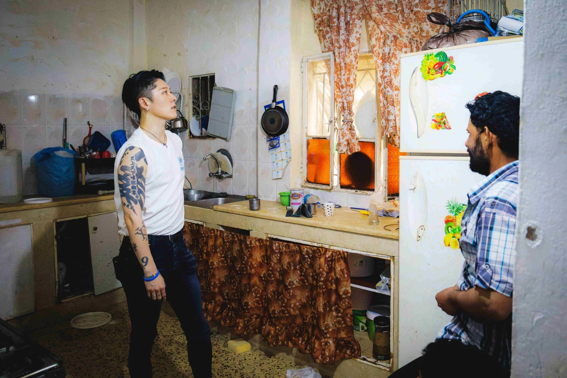 UNHCRロゴのTシャツを着たMIYAVI氏がキッチンで男性と向き合う