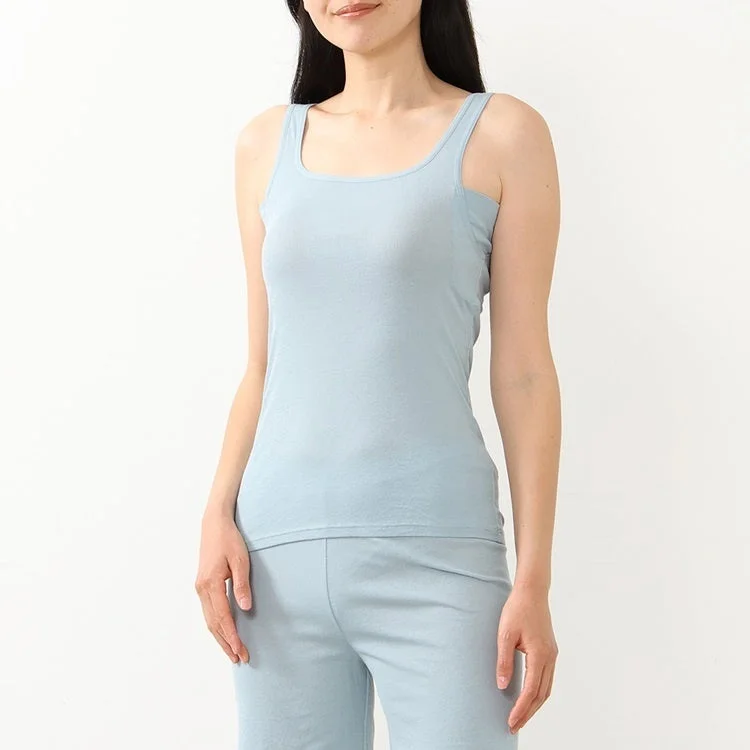 白い背景の前で、水色のタンクトップとパンツのセットアップを着用した女性が立っています
