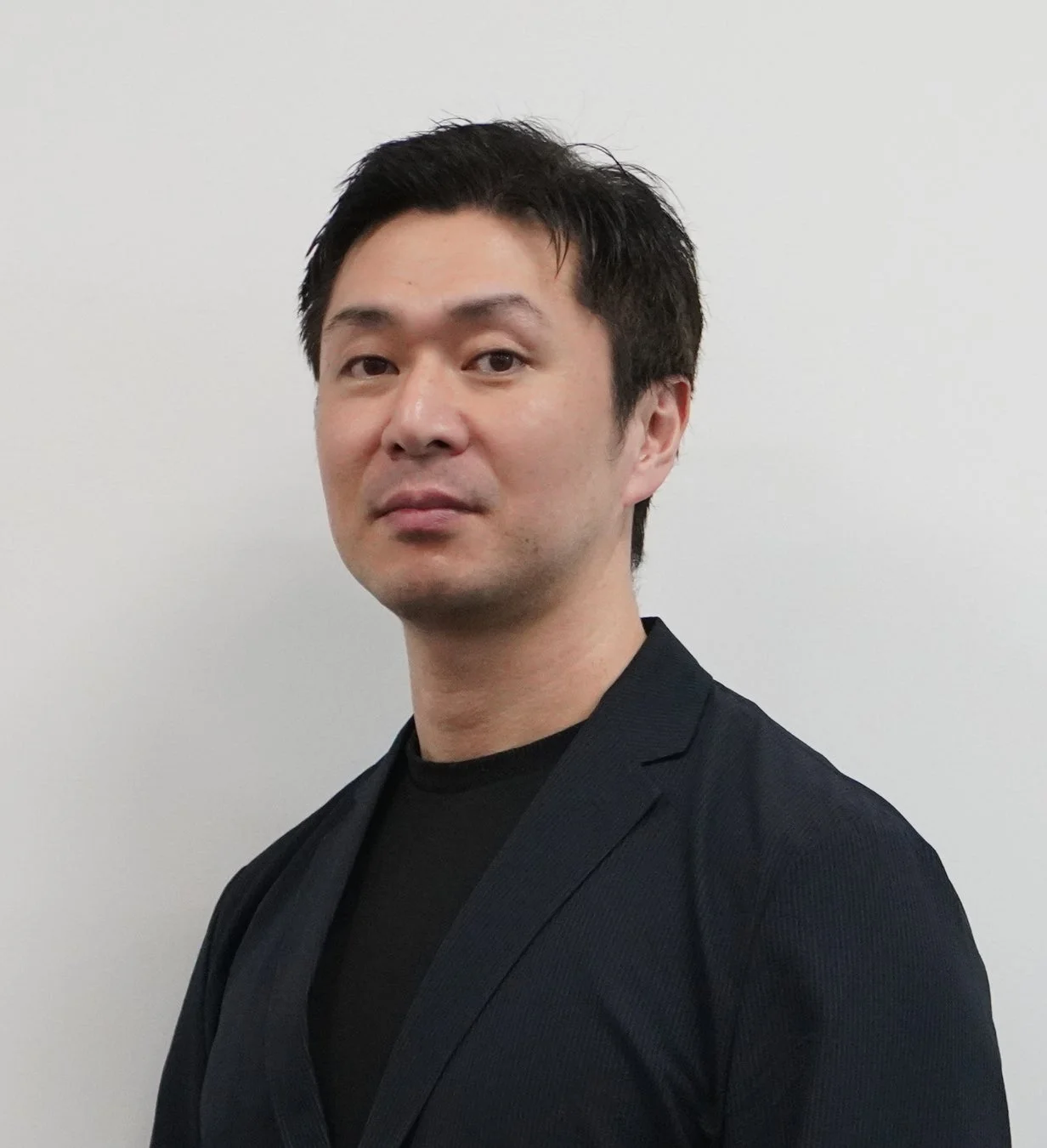 黒いTシャツとダークカラーのジャケットを着用した男性のポートレート