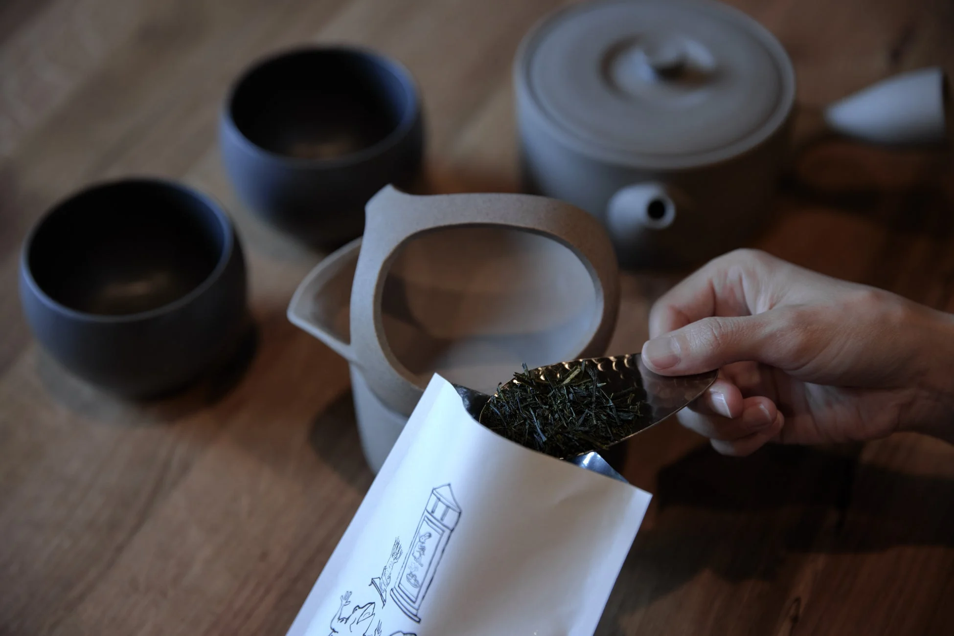 木目のテーブルの上で、手が茶葉を袋から茶器に移している