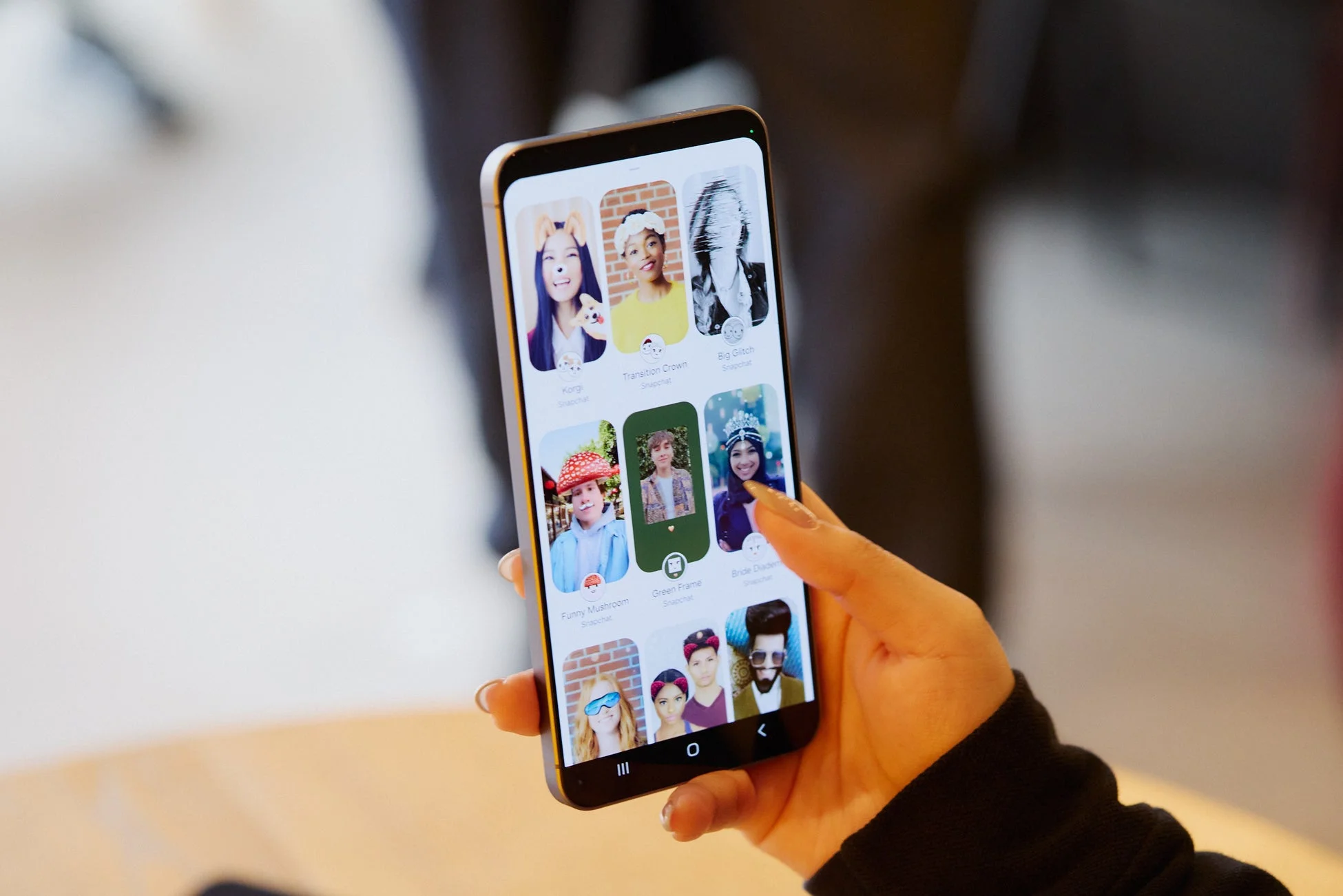 女性がスマートフォンを持ち、Snapchatアプリの様々なフィルターやレンズを閲覧している様子が写っています。画面には複数の人物が異なるエフェクトを適用された顔で表示されています。