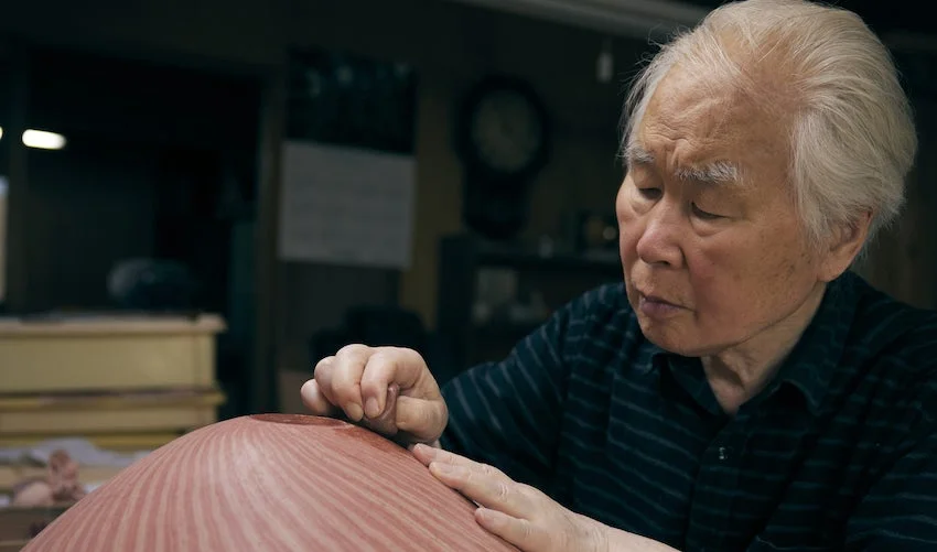 職人が木製の器のようなものに集中して手作業で加工している様子