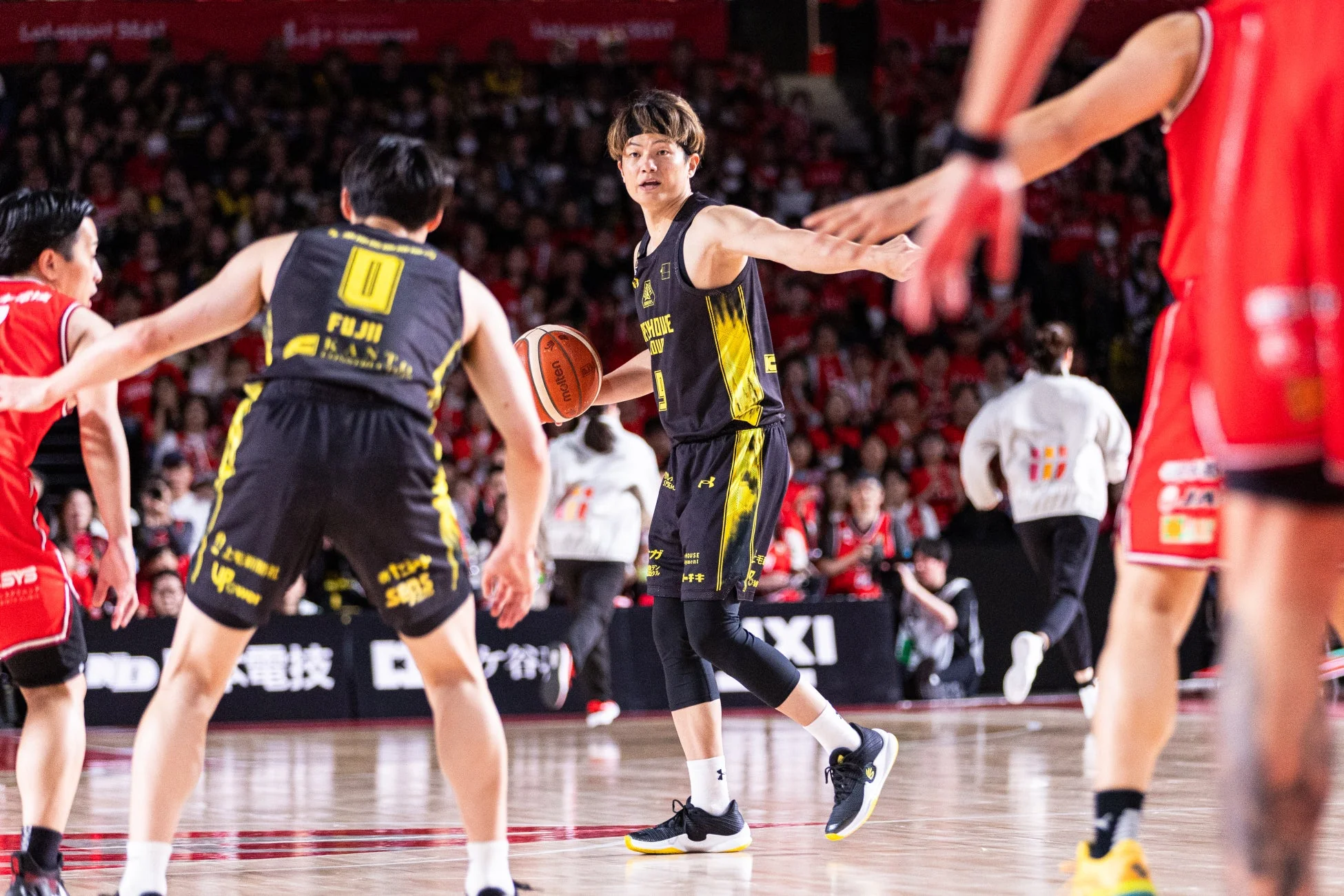 バスケットボールの試合で、黒と黄色のユニフォームを着た選手がボールを持ってコート中央に立っている