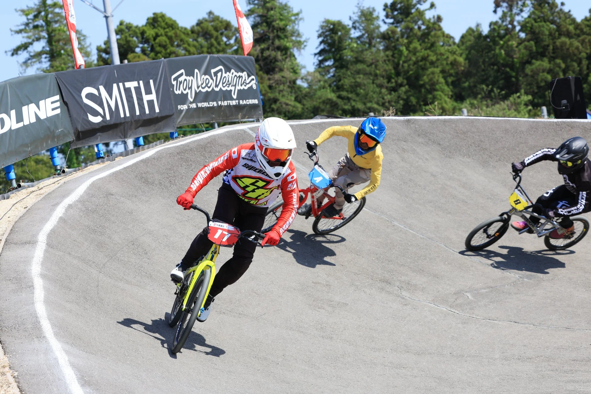晴れた屋外のBMXトラックで、3人の選手が自転車レースを繰り広げています