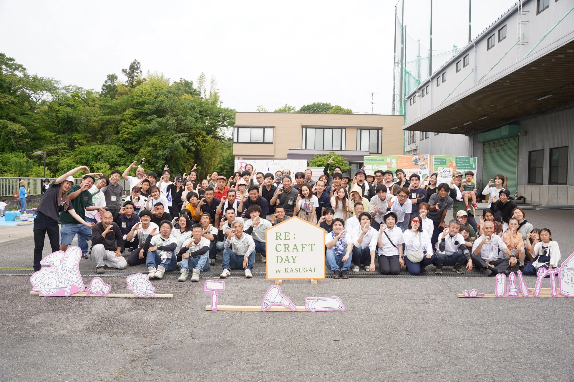 「RE:CRAFT DAY in KASUGAI」イベントに参加した大勢の人々が、笑顔でハートポーズを作っている集合写真
