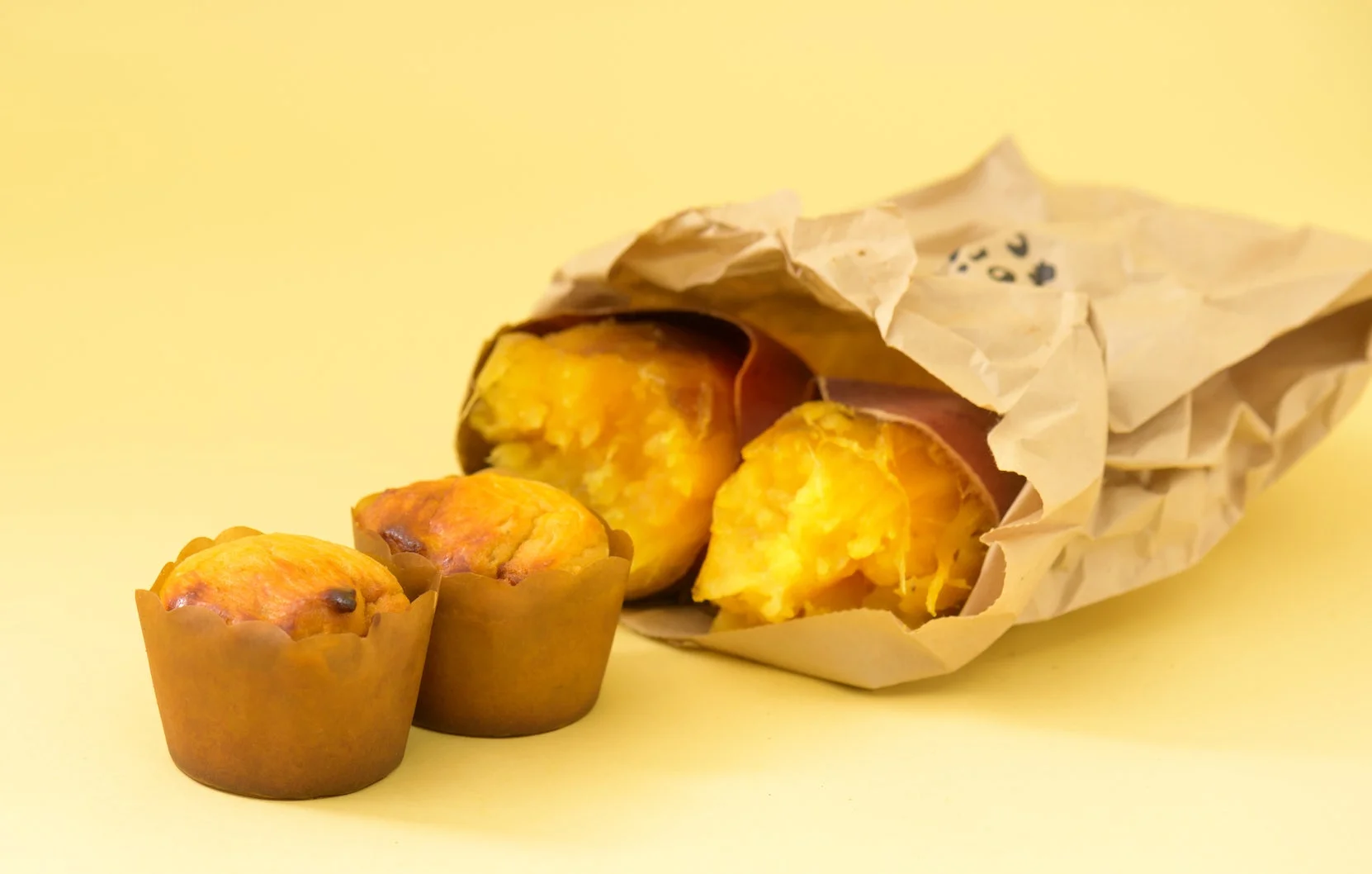 紙カップに入った2つのスイートポテトのようなお菓子と、茶色い紙に包まれた2つの焼き芋