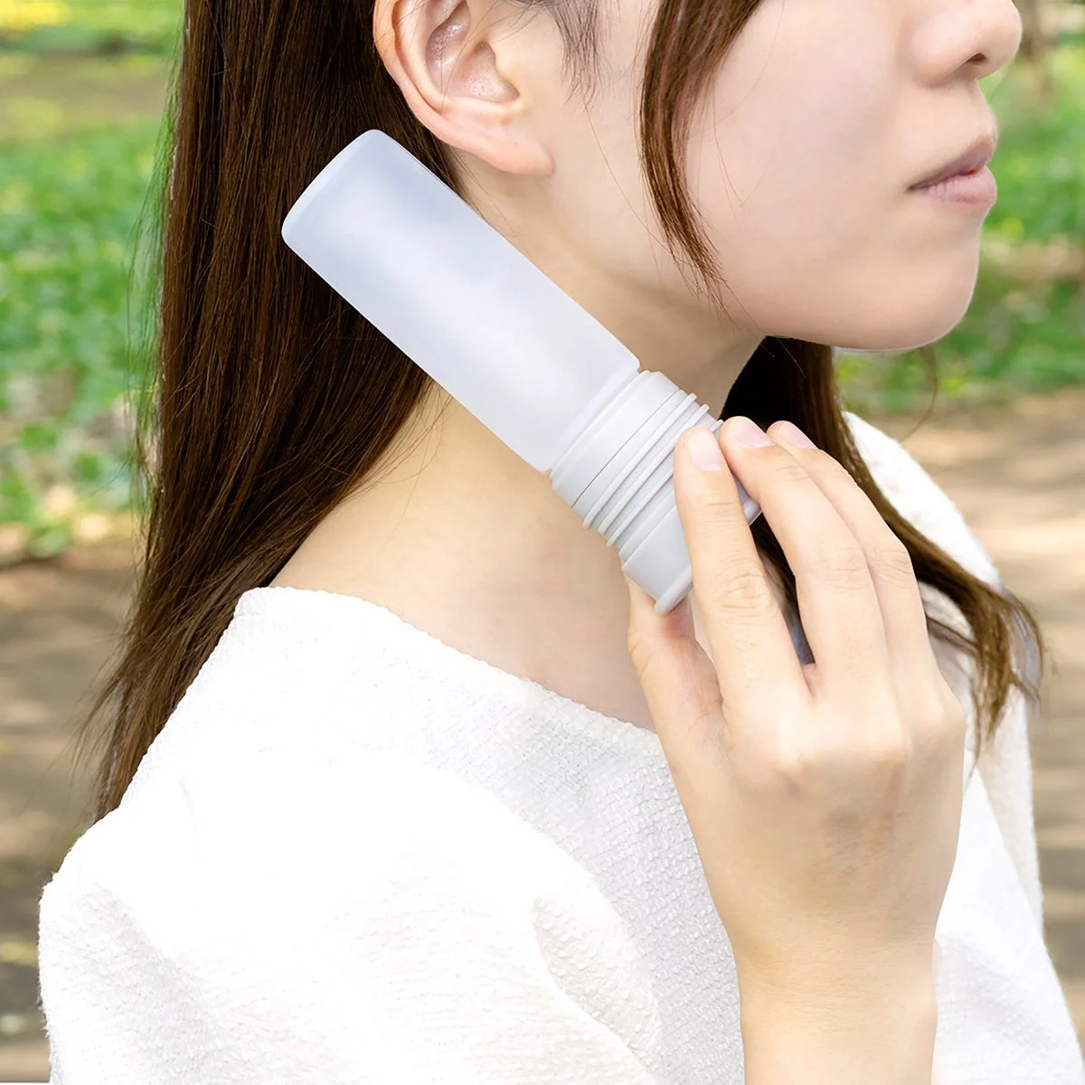 女性が屋外で半透明のボトルを首元に当てている様子
