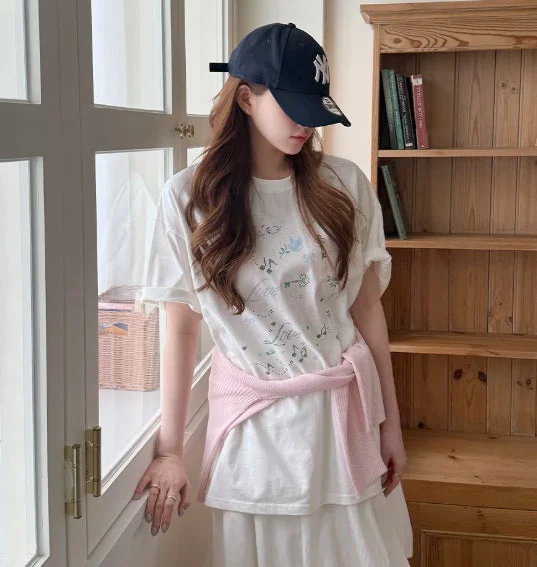 キャップとTシャツ、ピンクカーディガンの女性