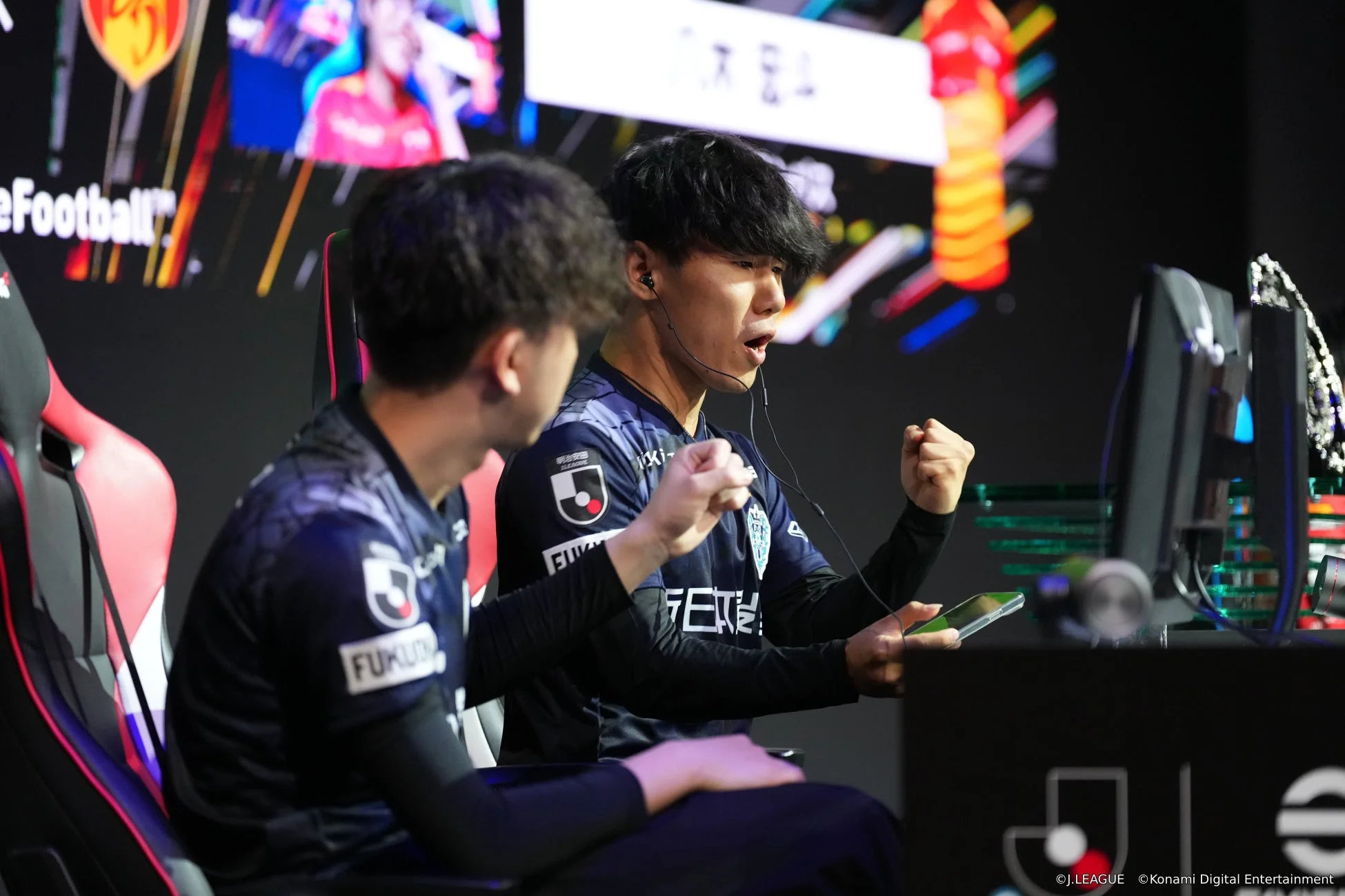 eスポーツの試合中に、Jリーグのユニフォームを着た選手がモニターに向かい、両手を握りしめ興奮している様子