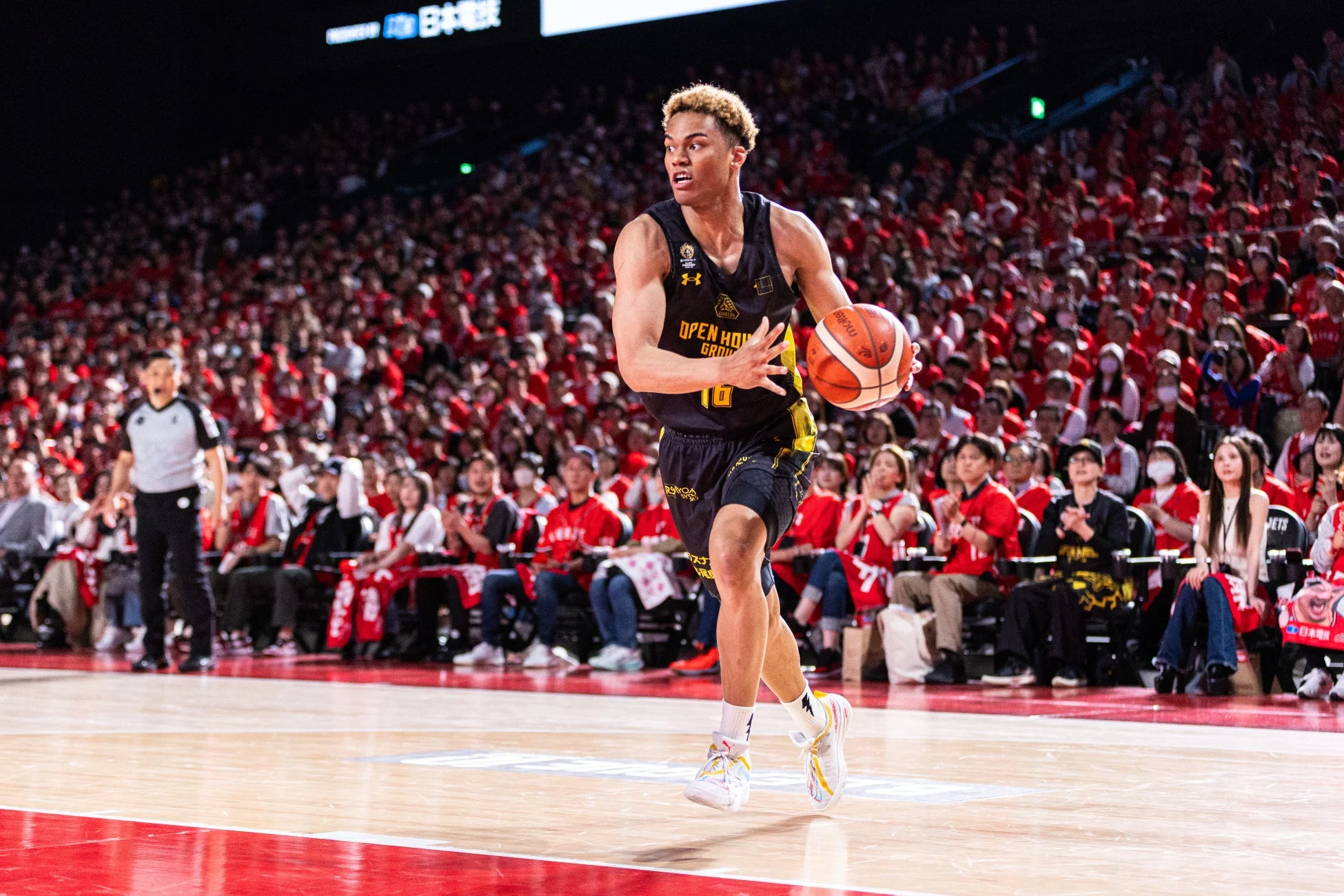 バスケットボールの試合中、背番号10の選手が黒と黄色のユニフォームを着てボールをドリブルしている