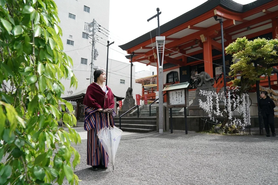 和装の女性が白い傘を持ち、日本の伝統的な神社を背景に立つ風景