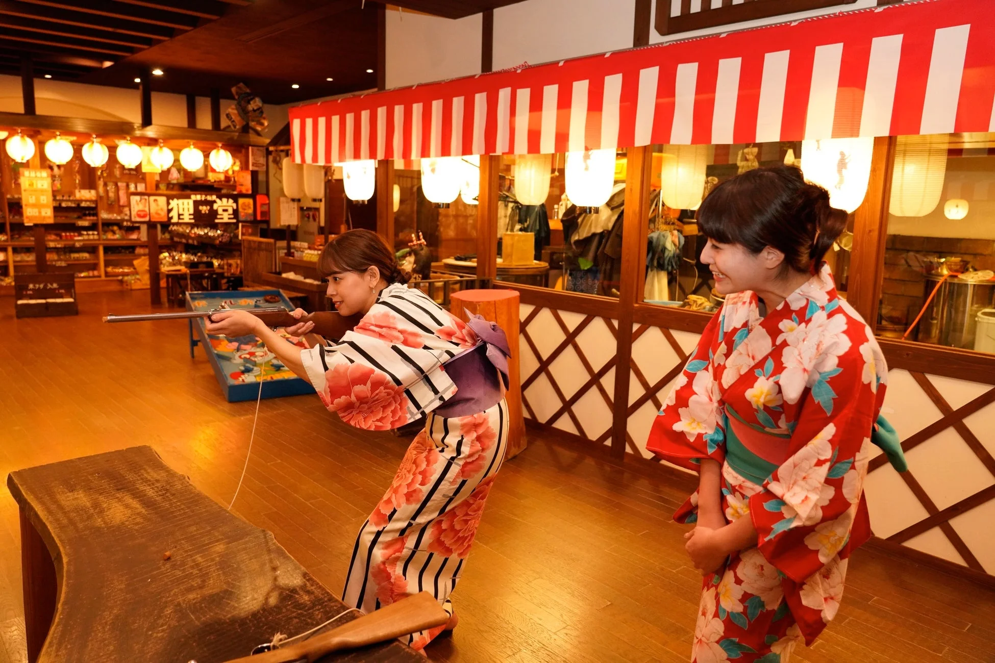浴衣を着た二人の女性が、日本の伝統的な射的ゲームを楽しむ様子