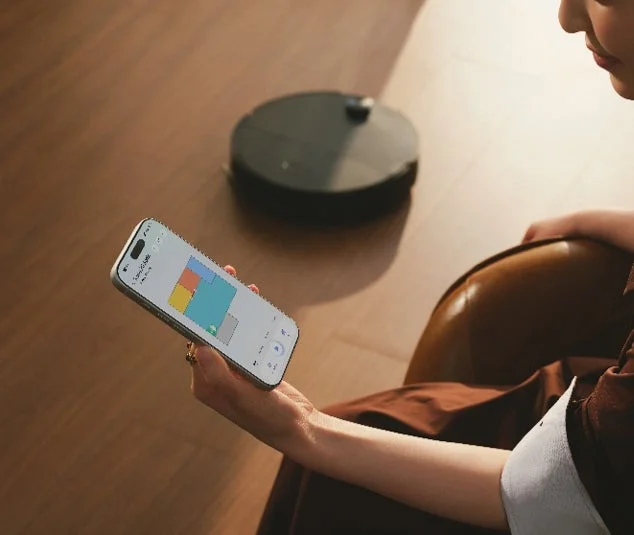 女性がスマートフォンを操作し、アプリでロボット掃除機を遠隔制御している様子