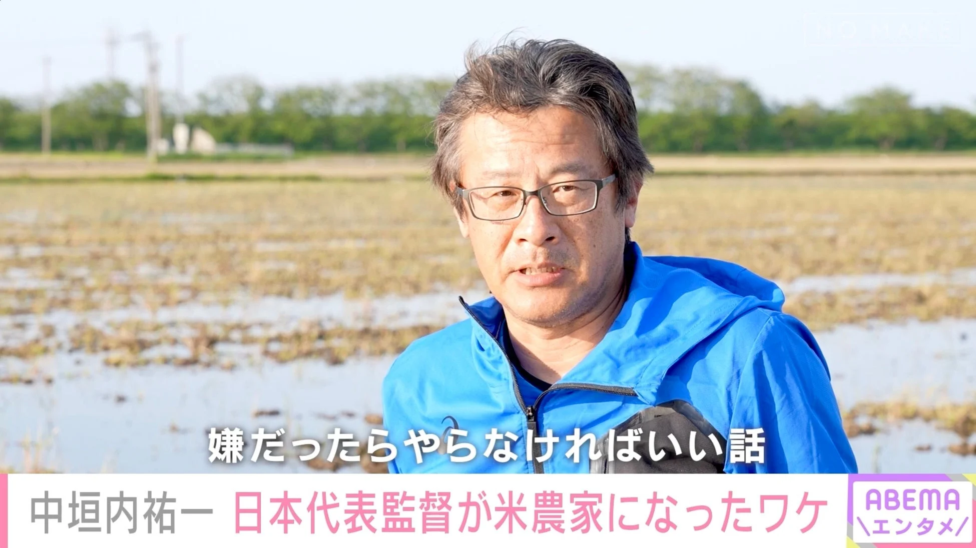 水田を背景に、青いジャケットを着た中垣内氏がカメラを見つめている画像