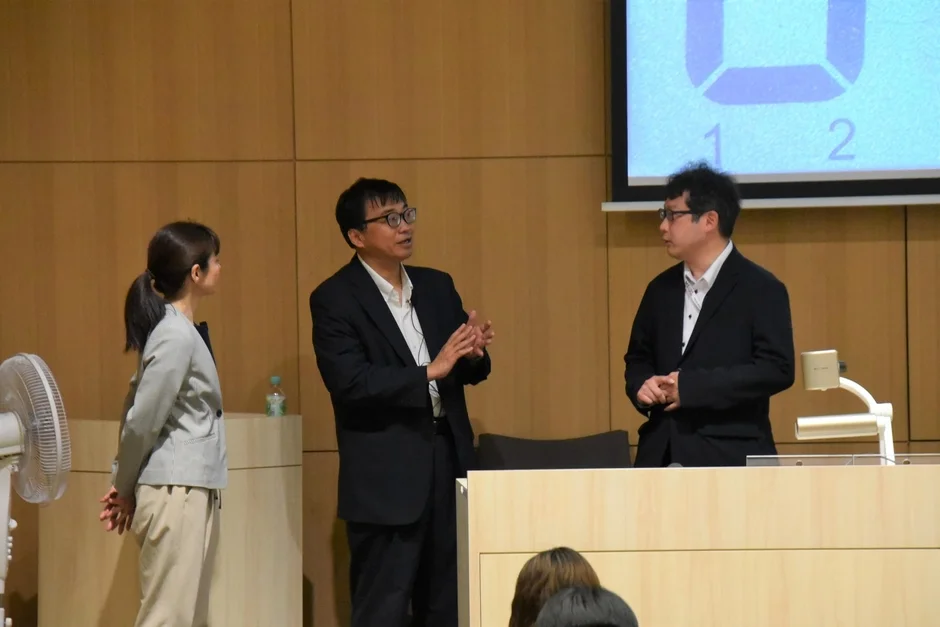 会議室で3人の男女がプレゼンテーションを行っている様子です。