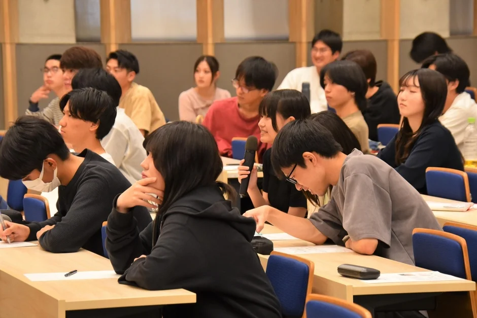 大学の講義室で、多くの学生が参加している様子です。