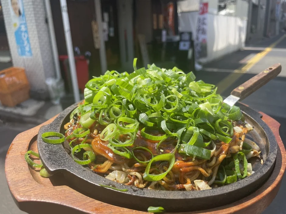 熱々の鉄板で提供される、たっぷりの青ネギが乗った香ばしい麺料理。