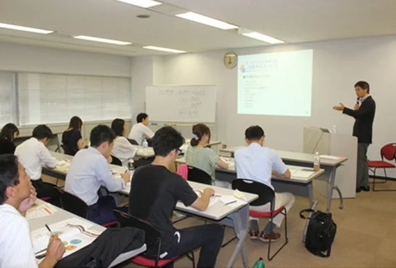 研修室で講師がプレゼンテーションを行い、受講者が耳を傾けている様子