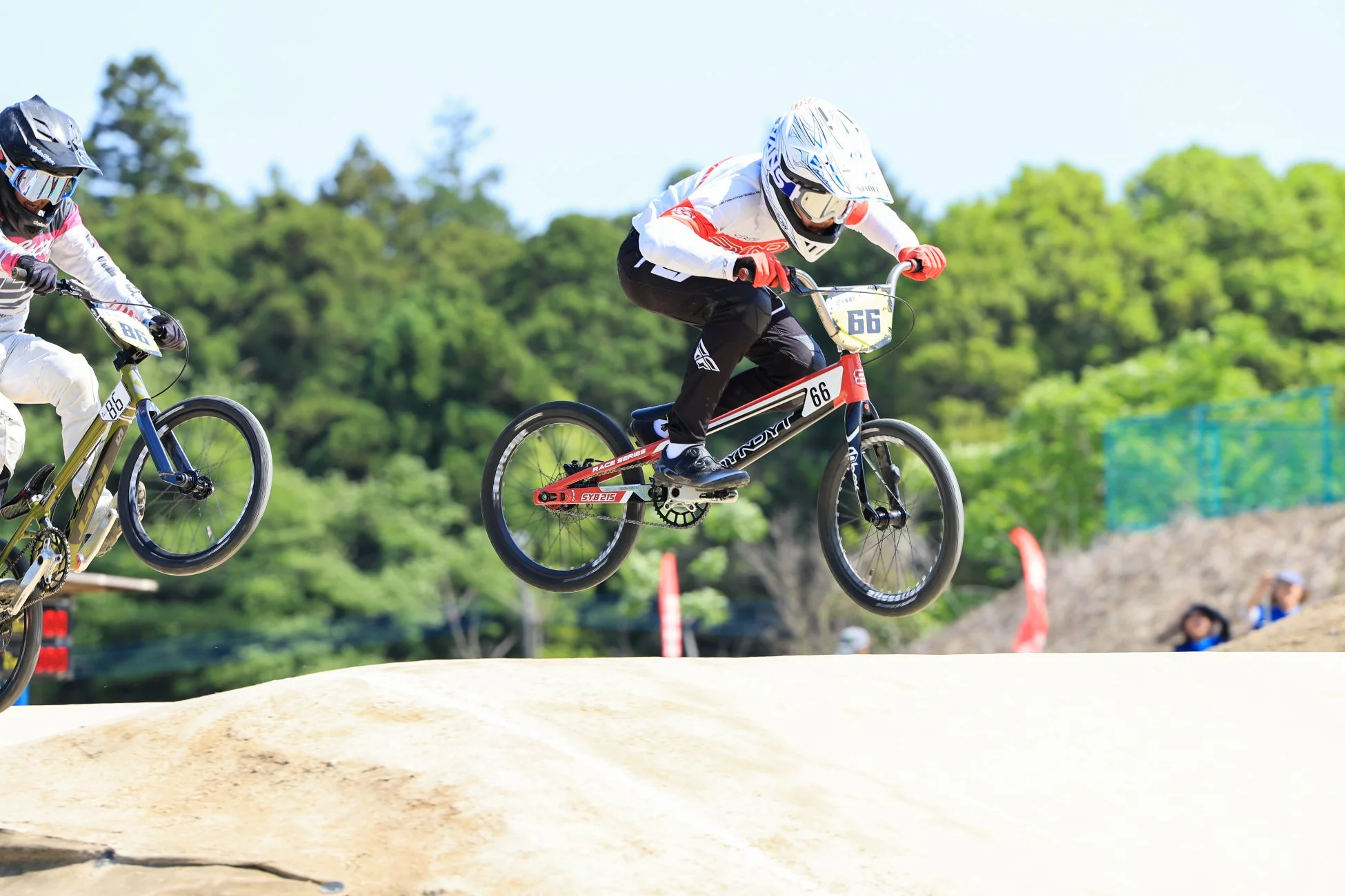 BMXレースで二人のライダーがオフロードコースのジャンプ台を飛び越えている瞬間