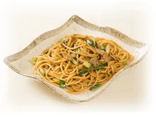 白い背景に、特徴的な白い皿に盛り付けられた温かい麺料理です。茶色い麺に豚肉と青菜が混ぜ込まれており、食欲をそそる焼きそばのような一品です。