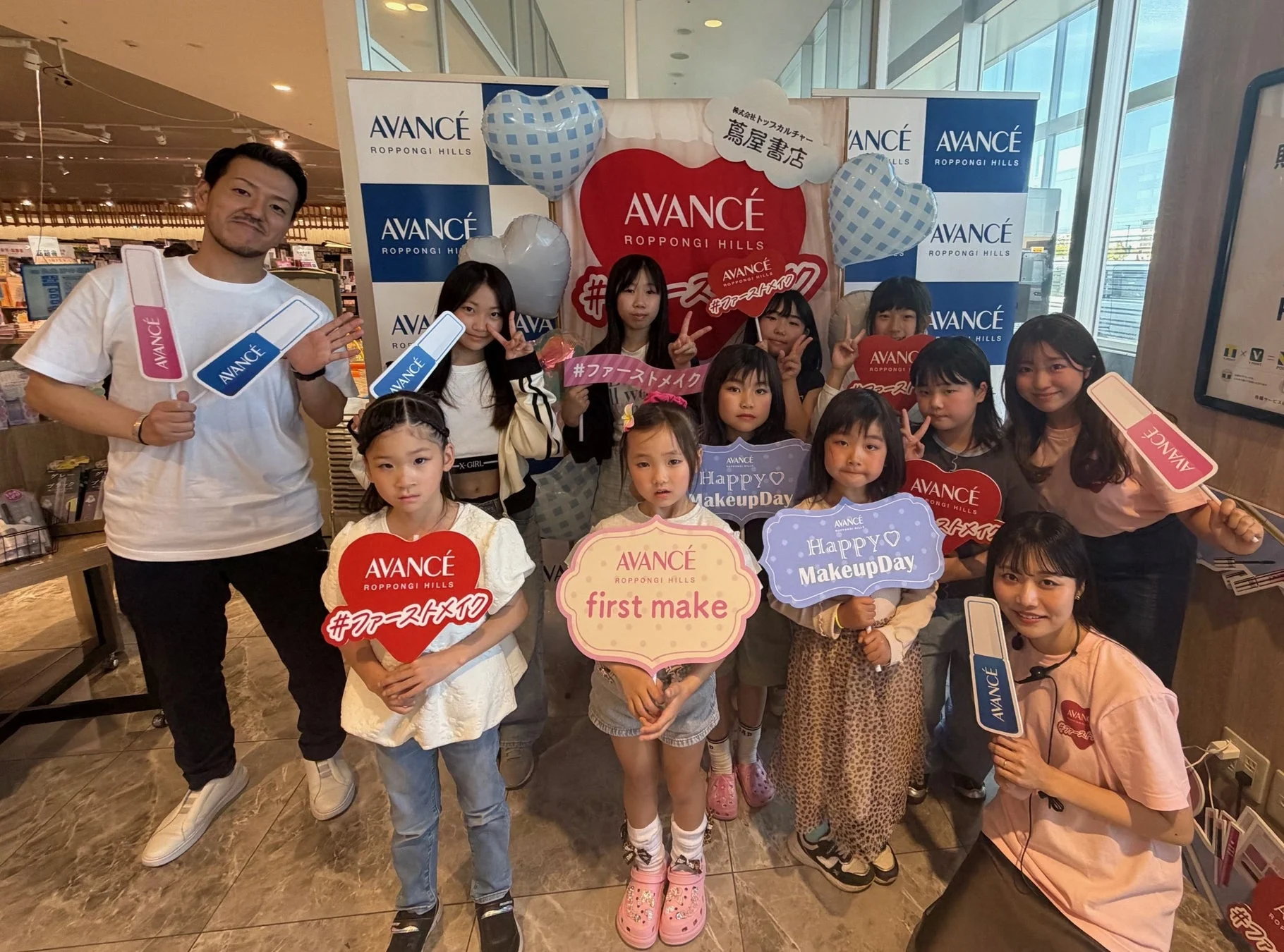 AVANCÉ ROPPONGI HILLSが主催したメイクイベントの集合写真です。子供たちが「ファーストメイク」や「Happy Makeup Day」と書かれたボードを持ち、楽しそうにポーズをとっています。蔦屋書店とのコラボレーションイベントのようです。
