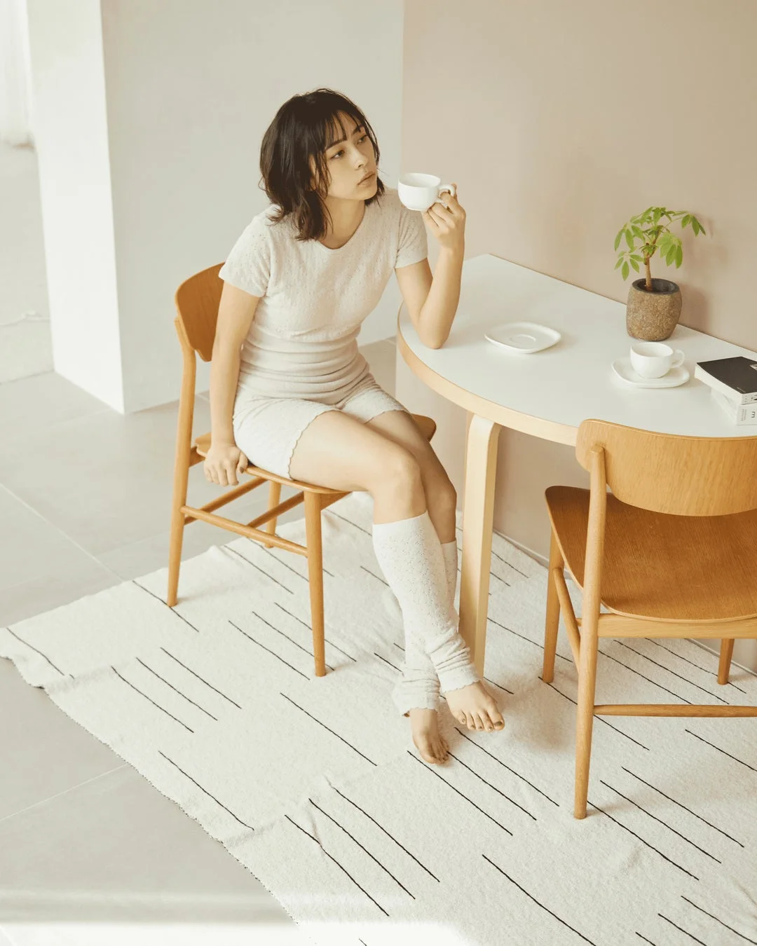明るい部屋で女性がテーブルに座り、コーヒーカップを手にリラックスしている様子