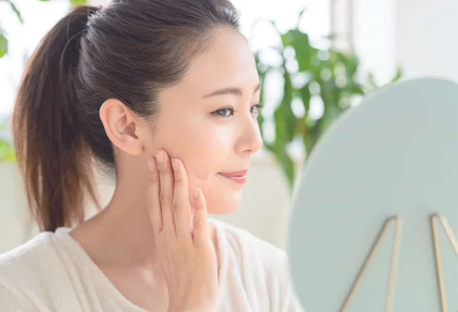 鏡を見ながら頬に何かを塗っている女性の姿