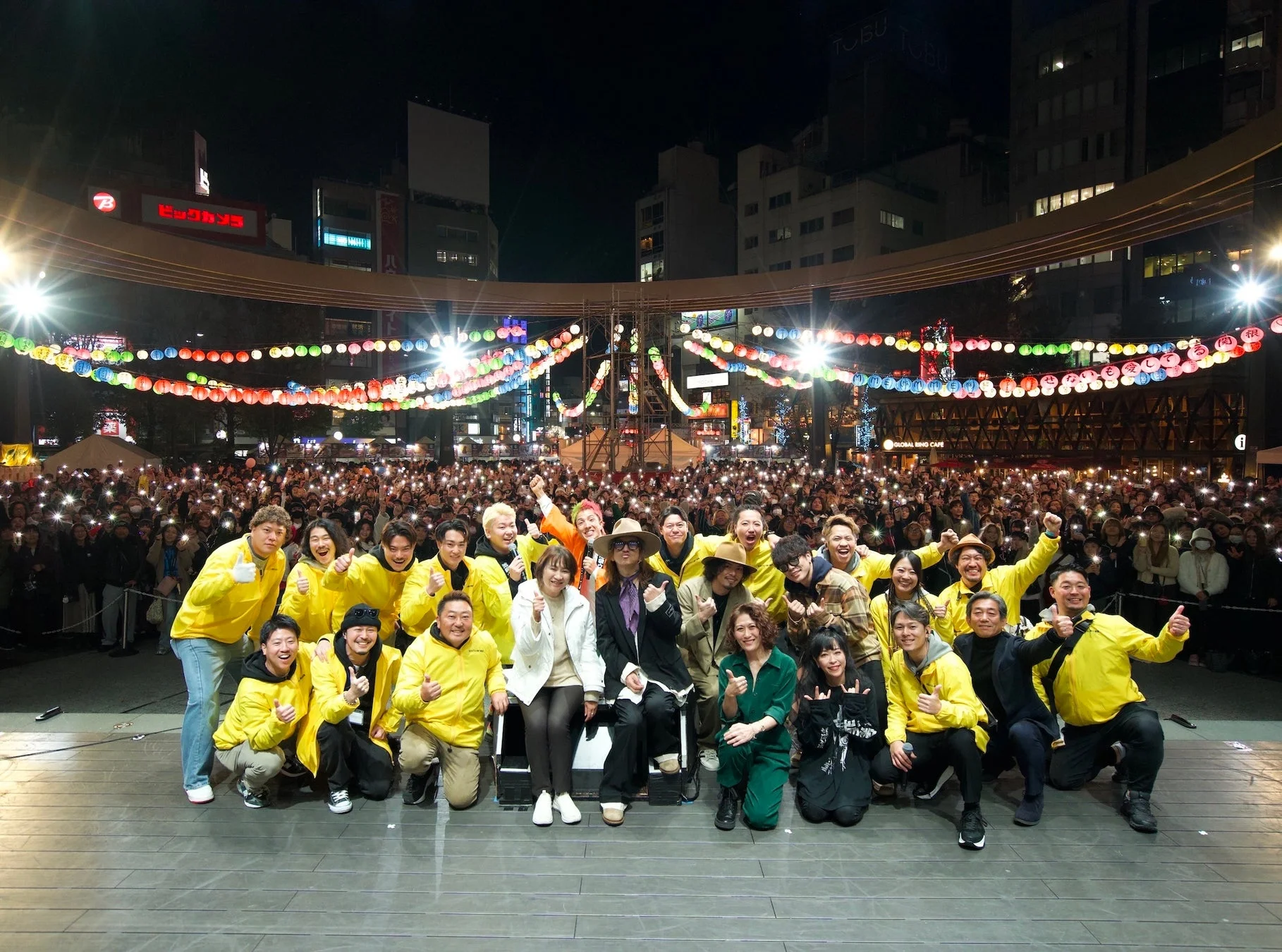 夜の広場で開催されたイベントでステージに立つ出演者たち