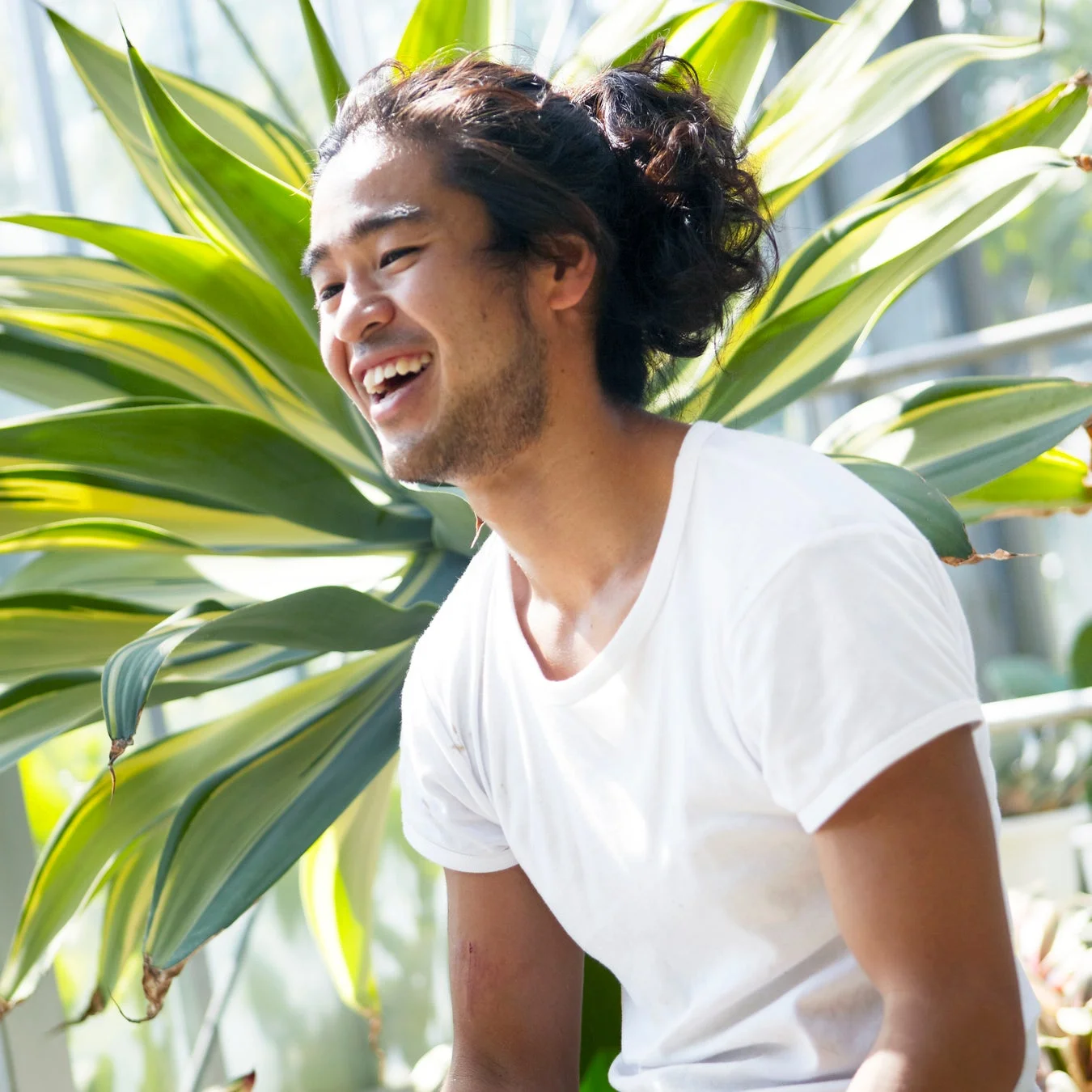 大きな葉の植物を背景に、白いTシャツを着た男性が満面の笑みを浮かべているポートレート写真