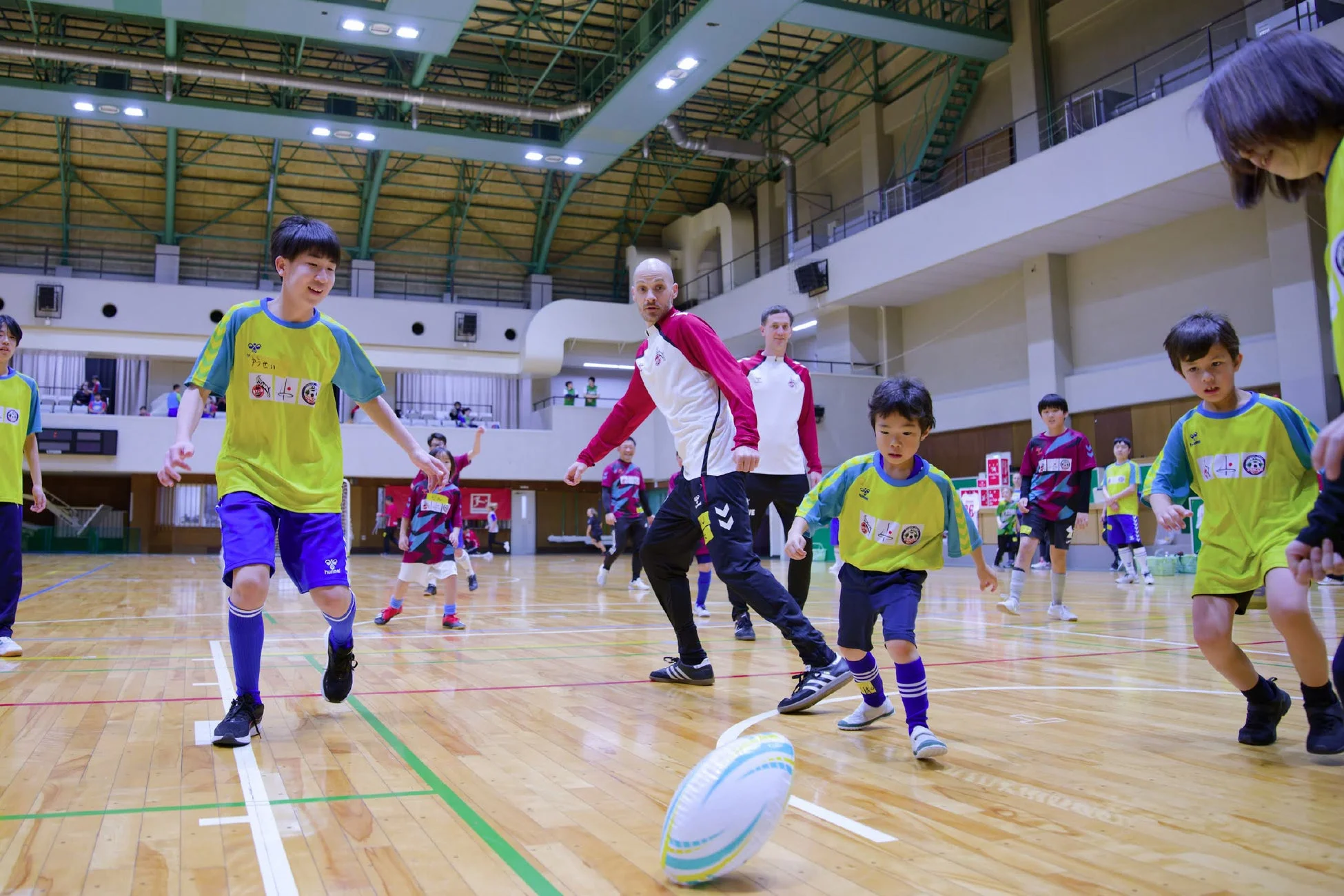 体育館で子供たちがラグビーボールを囲んで楽しそうに活動している様子