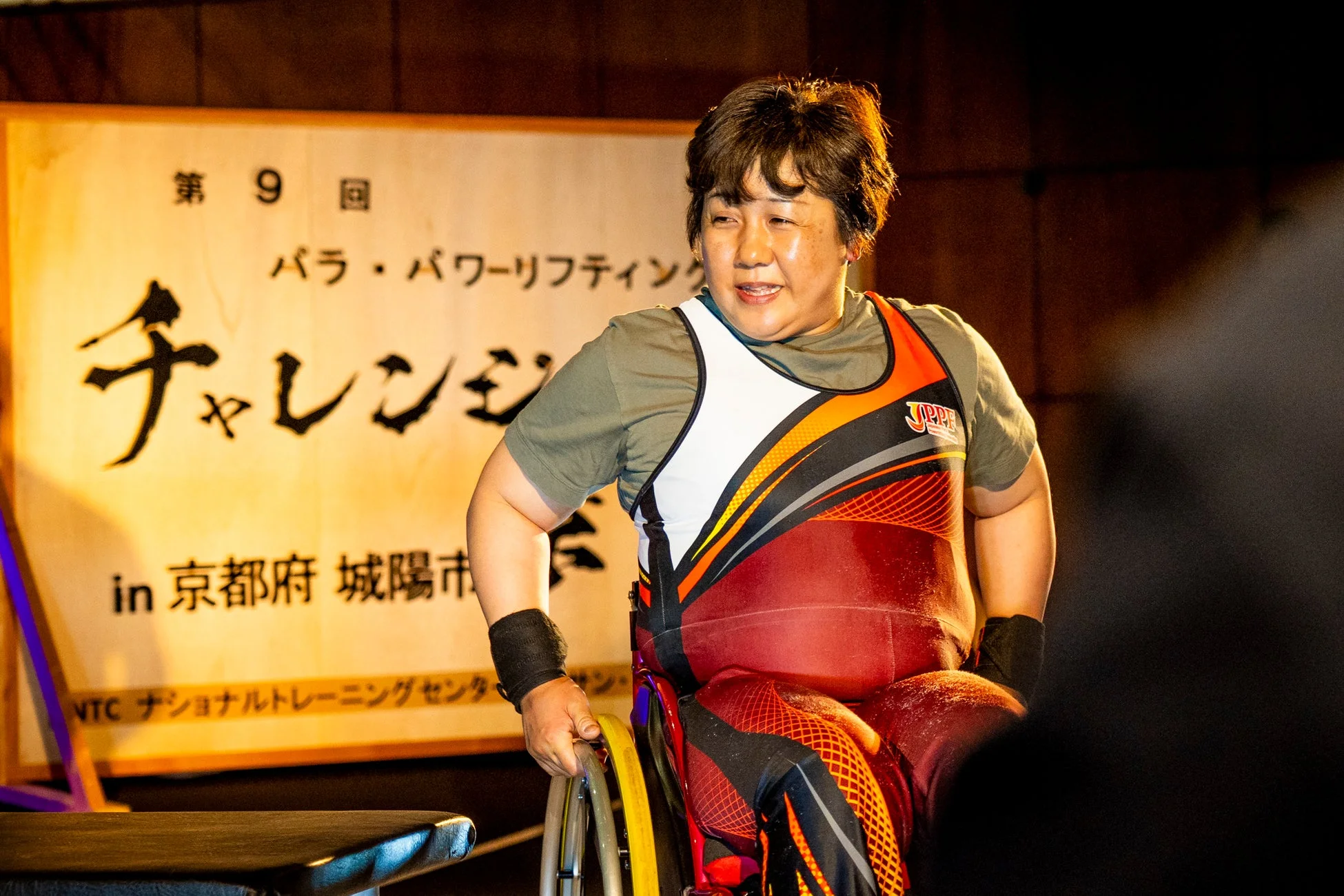 車椅子に乗った女性パラパワーリフティング選手が、第9回パラ・パワーリフティングチャレンジの会場で笑顔を見せています。