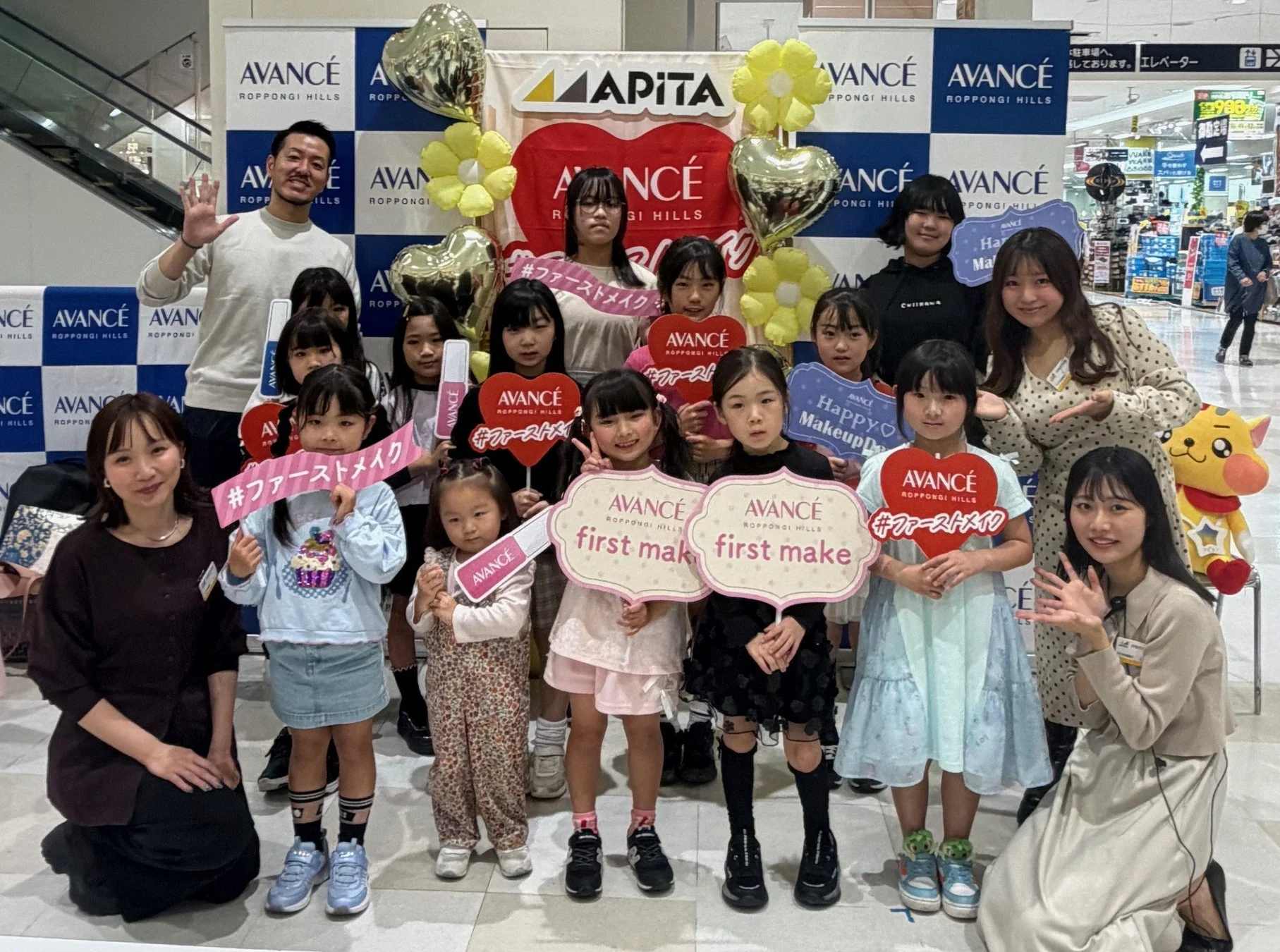「AVANCÉ ROPPONGI HILLS」と「APITA」のイベントで、子供たちが初めてのメイクを体験している集合写真です。大人たちも一緒に笑顔でポーズをとっており、和やかな雰囲気が伝わります。