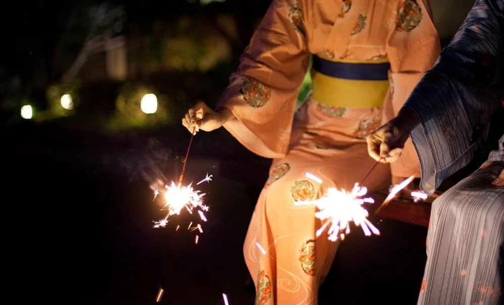 夜の屋外で、浴衣を着た二人が線香花火を楽しんでいる様子