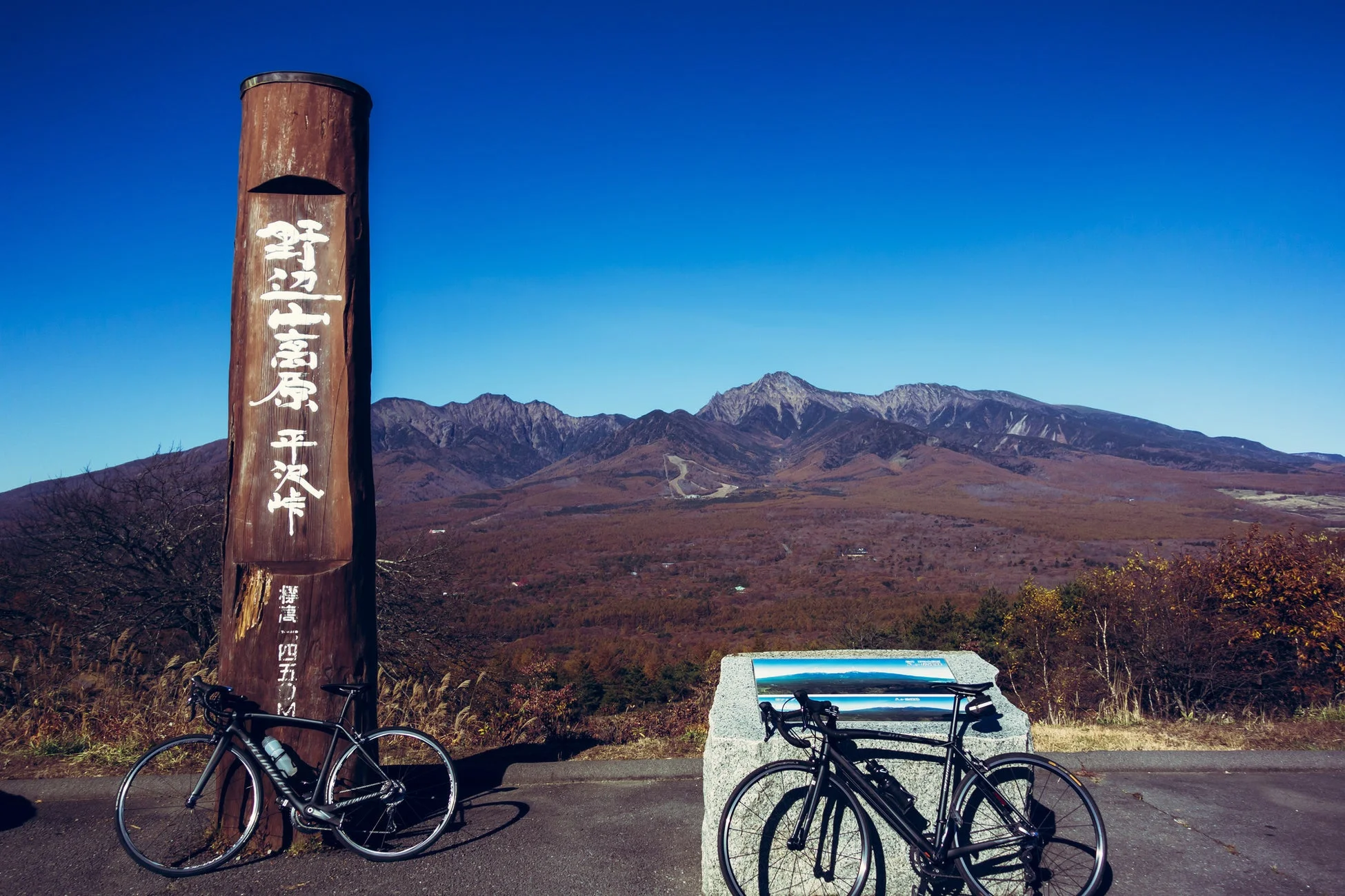 晴れた青空の下、野辺山高原平沢峠の展望台で撮影された写真。二台のロードバイクが停車しており、広がる高原と遠くの山々が美しい景色を作り出している。