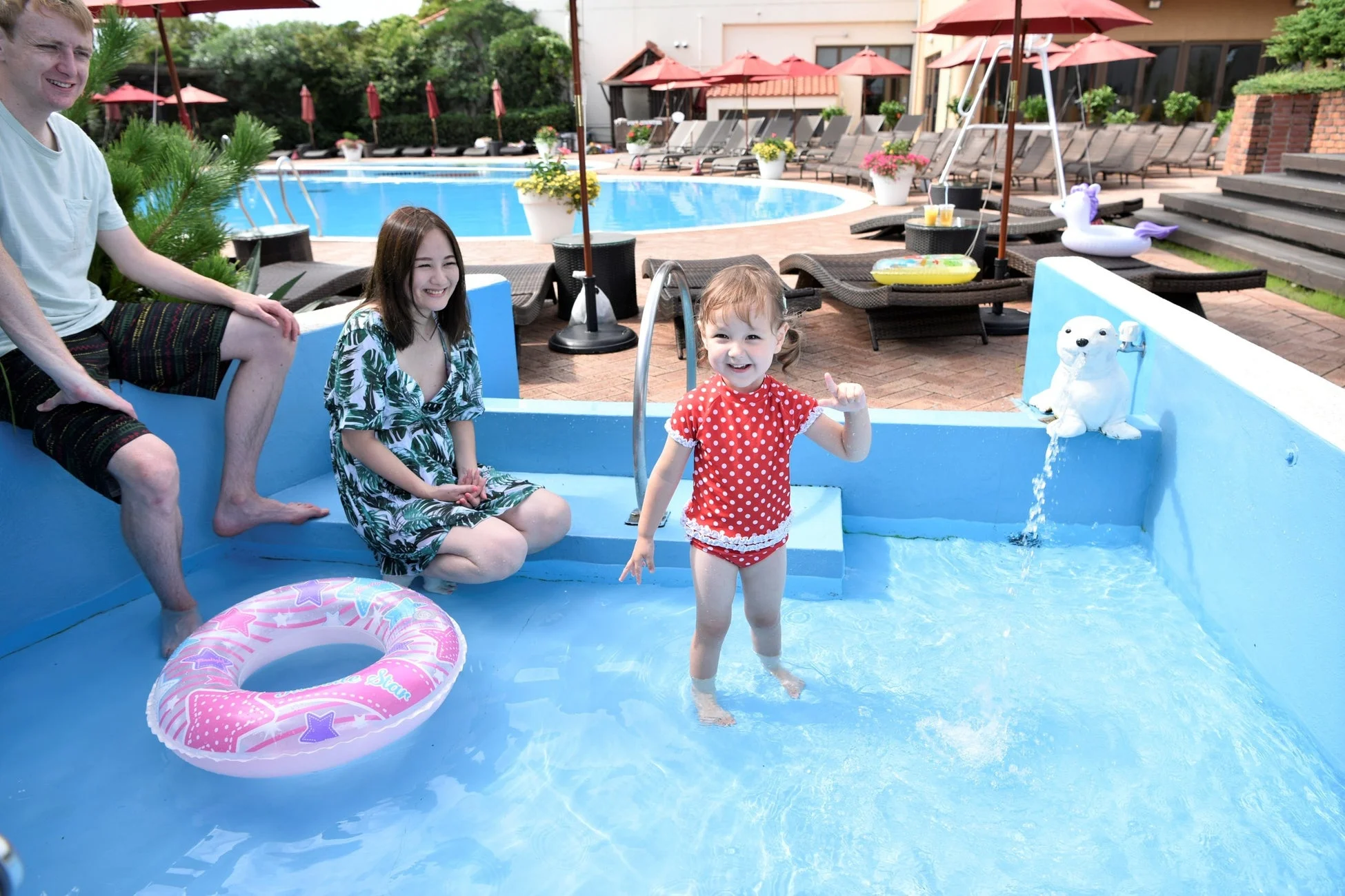 リゾートホテルのプールサイドで水遊びを楽しむ幼い女の子と両親