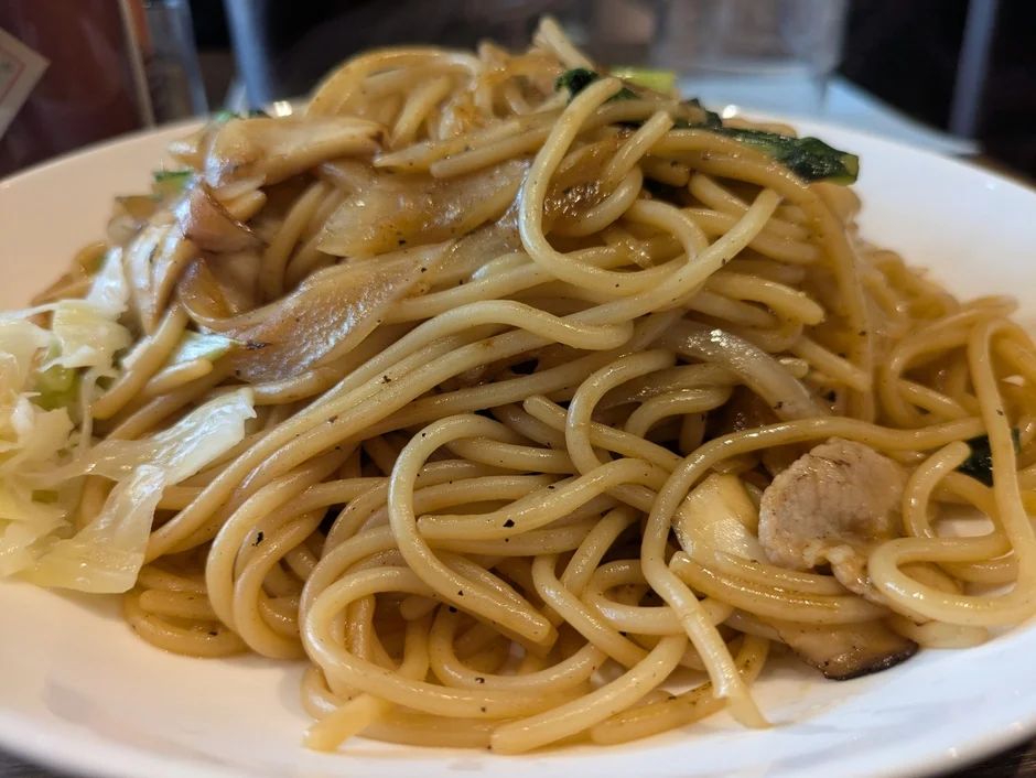 皿に盛られた具だくさんの焼きそば風パスタです。キャベツ、玉ねぎ、きのこ、肉などが入り、香ばしく炒められており、食欲をそそる一品です。