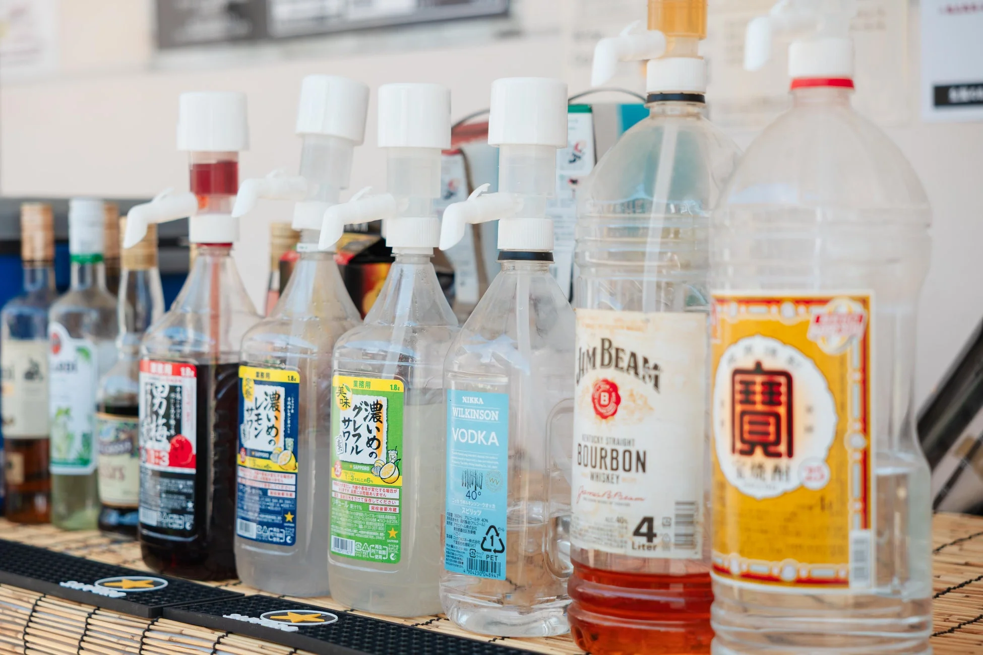 居酒屋やイベントで使われるような、様々な種類の酒瓶とサワーの素が並べられたカウンターの様子。ディスペンサーが取り付けられたボトルもあり、手軽にドリンクが作れる準備がされています。