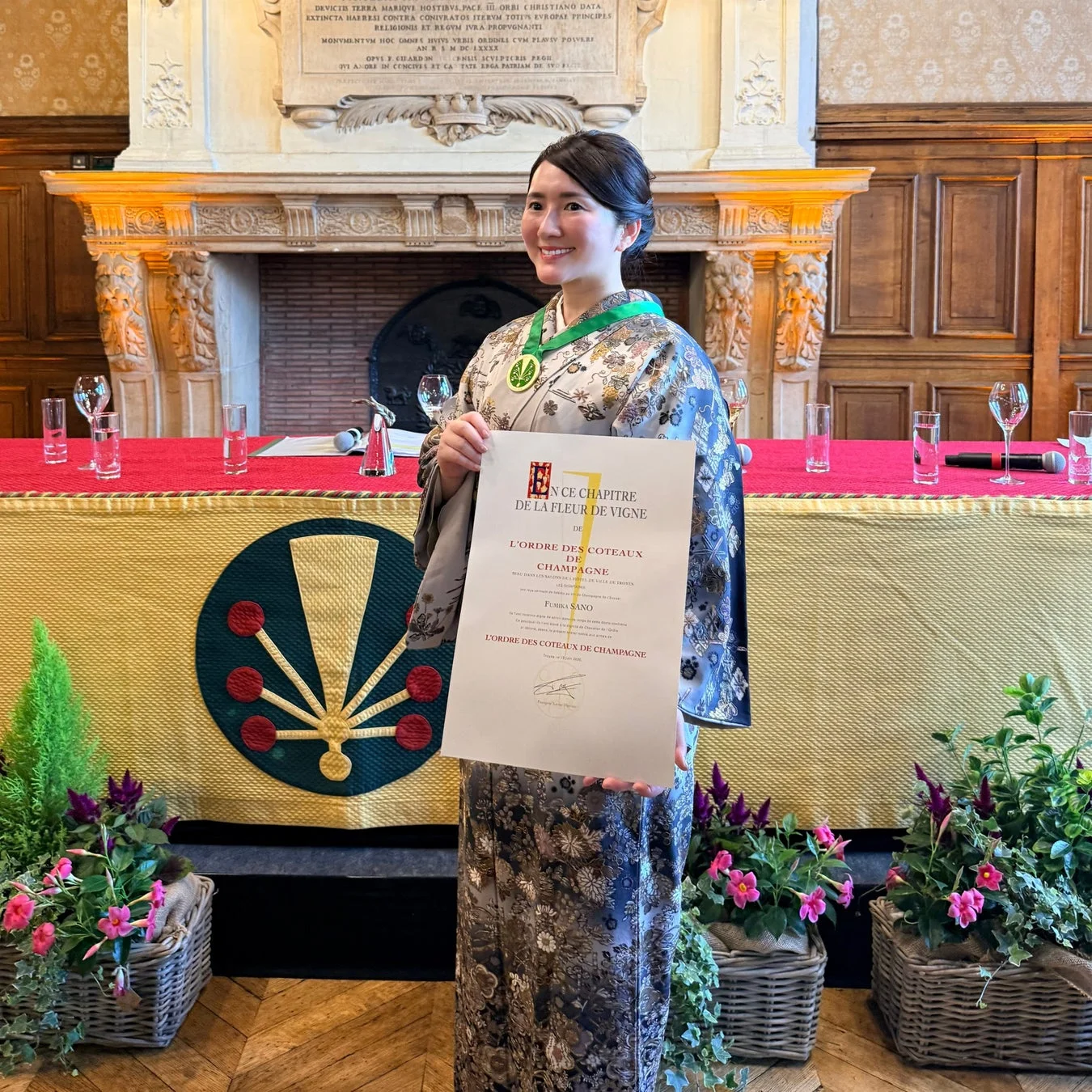 着物姿の女性が、シャンパーニュ地方のワイン騎士団の認定証を持ち、笑顔で立つ一枚