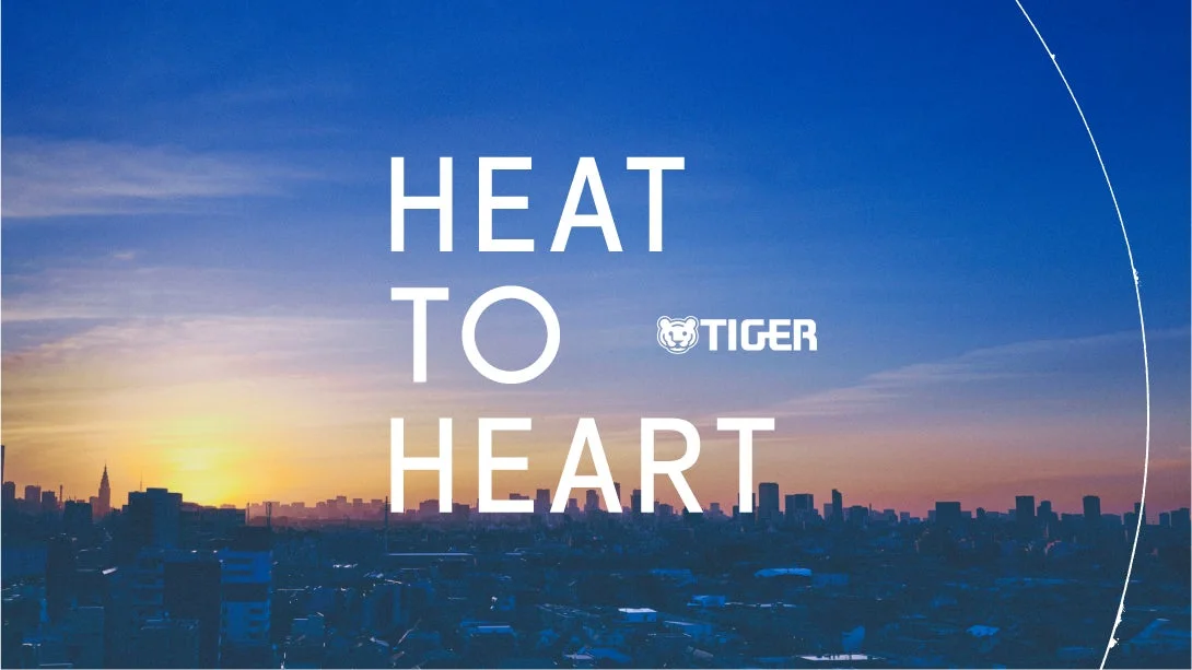 夕暮れの街のスカイラインを背景にした「HEAT TO HEART」ロゴ