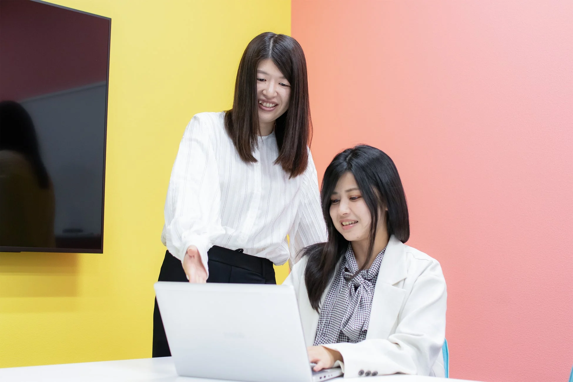 明るいオフィスでノートパソコンを囲んで笑顔で打ち合わせをする二人の女性