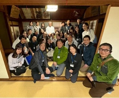 大人数のグループが伝統的な和室に集まり、笑顔で集合写真に収まっています。和やかな雰囲気のイベントや交流会の様子がうかがえます。