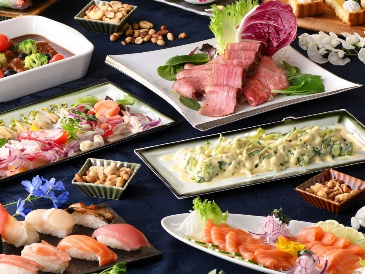 豪華な食卓に、寿司、刺身、ローストビーフ、サラダ、煮込み料理など、多種多様な料理が美しく並べられています。パーティーや宴会にぴったりの華やかで豊かな食事風景です。