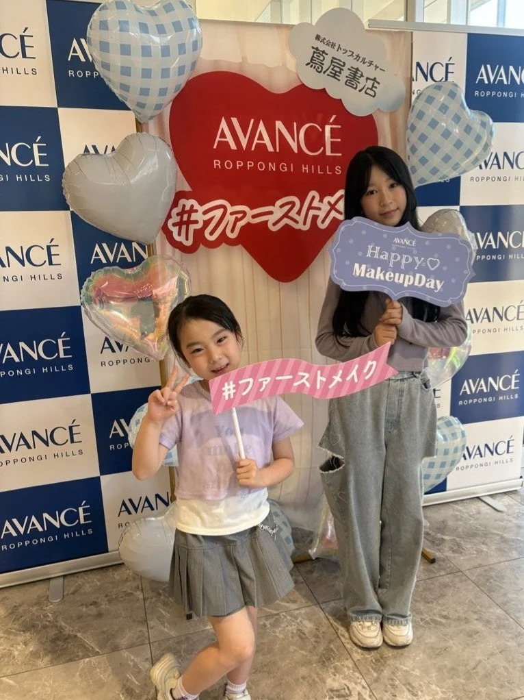 「AVANCÉ ROPPONGI HILLS Happy Makeup Day」イベントで、2人の女の子がハートのバルーンやロゴを背景に笑顔でポーズをとっています。初めてのメイク体験を楽しむ様子が伝わる可愛らしい一枚です。