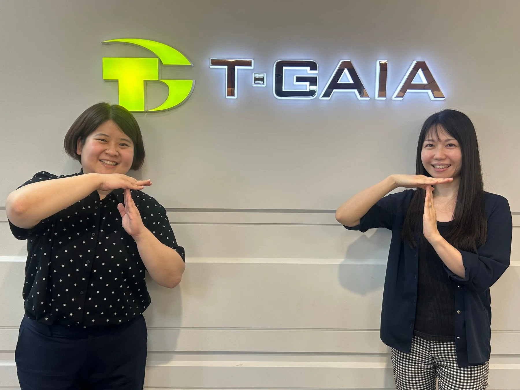 T-GAIAのロゴを背景に笑顔の女性従業員