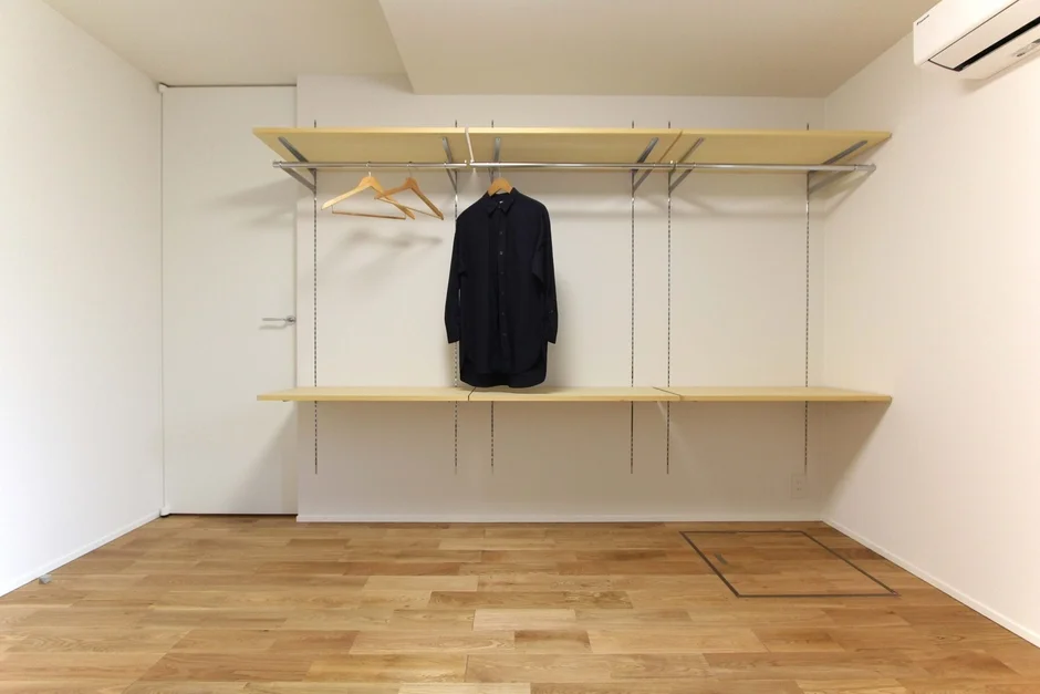 白い壁と木製フローリングのシンプルな部屋に、オープンタイプのクローゼットが設置されています