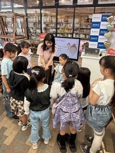店内で、女性が子供たちに何かを教えているワークショップの様子。画面には「Let's try!!」と表示され、美容ブランドAVANCEのロゴも見られることから、子供向けの美容やスキンケアに関するイベントだと考えられます。