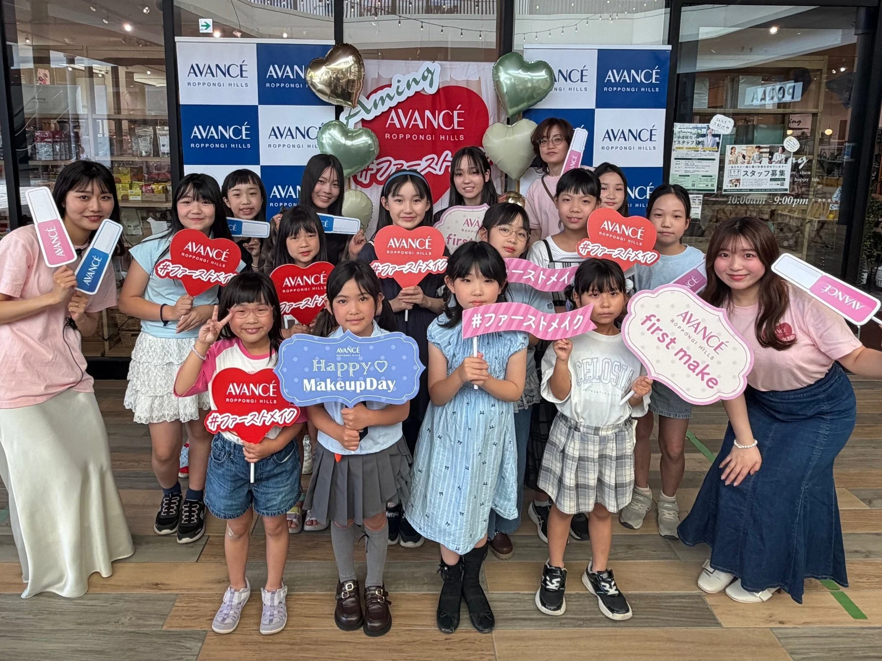AVANCÉ六本木ヒルズのイベントで、多くの子供たちが大人と一緒に「ファーストメイク」や「Happy Makeup Day」と書かれたボードを持って笑顔でポーズをとっている集合写真。