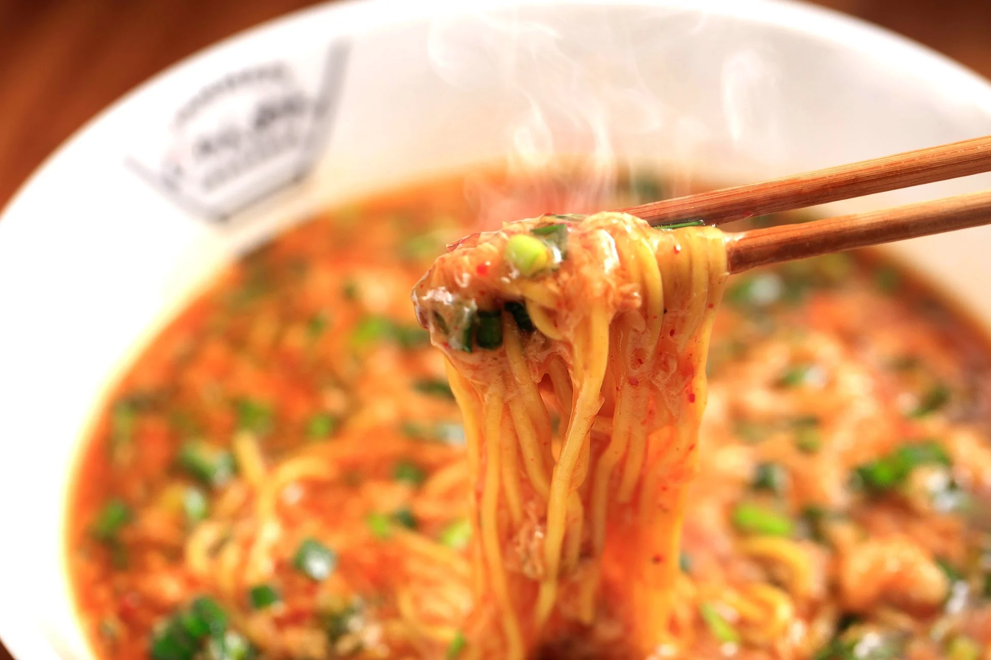 湯気を立てる熱々のラーメンを箸で持ち上げているクローズアップ写真です。
