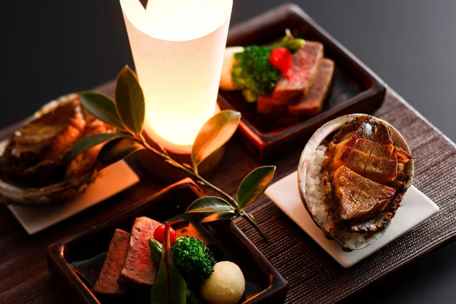 高級感のある和風の膳に、アワビの炊き込みご飯や牛肉料理などが美しく盛り付けられている